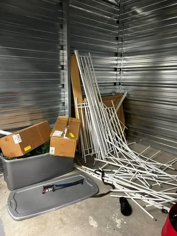 A storage unit filled with unused boxes, disorganized metal pipes, and other clutter, awaiting a cleanout.