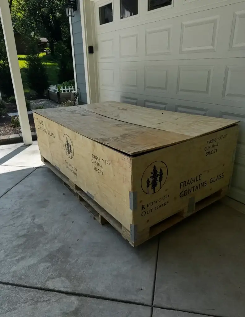 A large wooden crate with fragile glass markings sitting outside a garage.