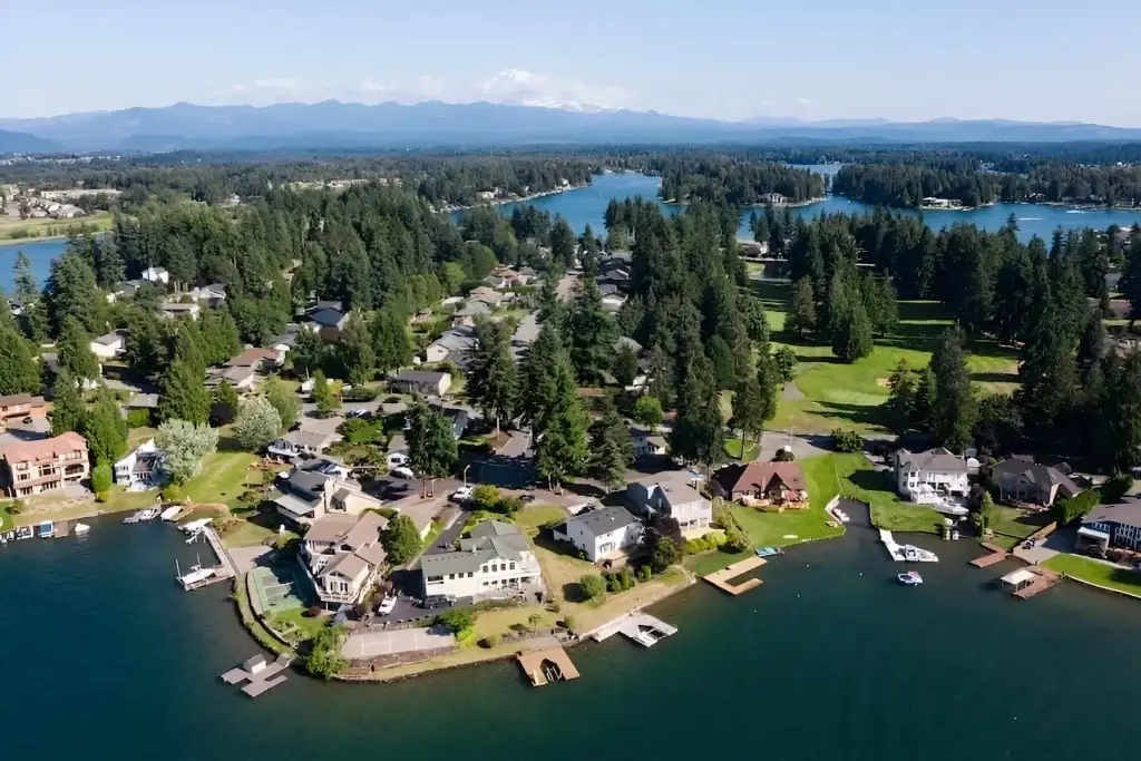 Aerial view of Bonney Lake, WA, showing peaceful waterfront homes, docks, and lush greenery, with mountains in the distance. Junk Removal in Bonney Lake WA services available.