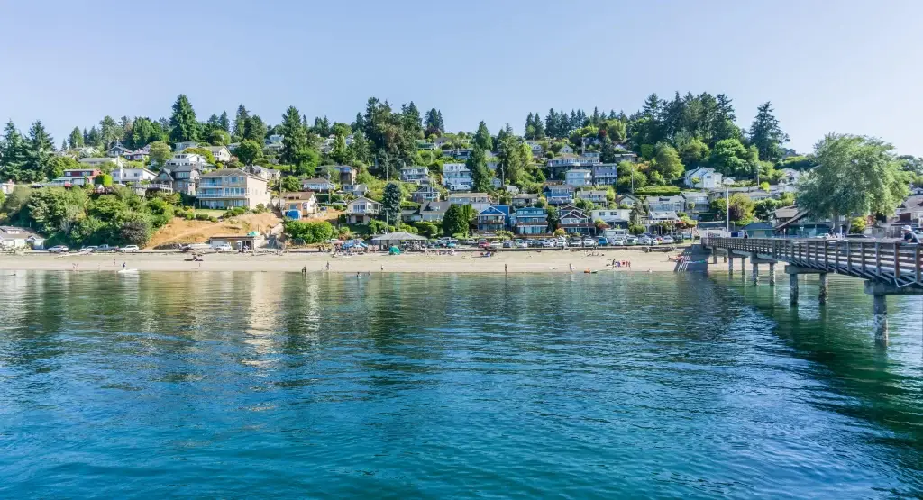 A beautiful view of Dash Point, WA, featuring waterfront homes, a sandy beach, and a pier extending into the water, with Junk Removal in Dash Point, WA services available.