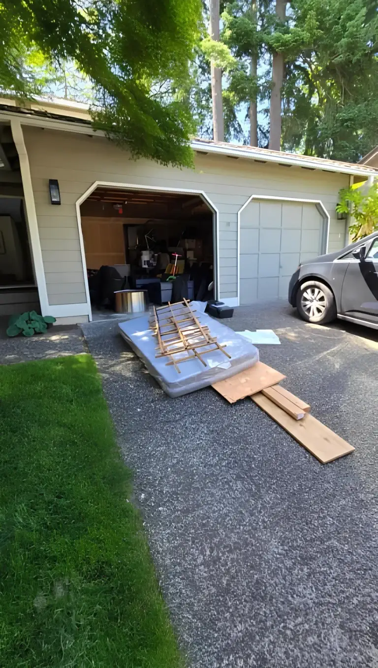 Old mattress and wooden planks placed outside an open residential garage ready for mattress disposal Seattle services.